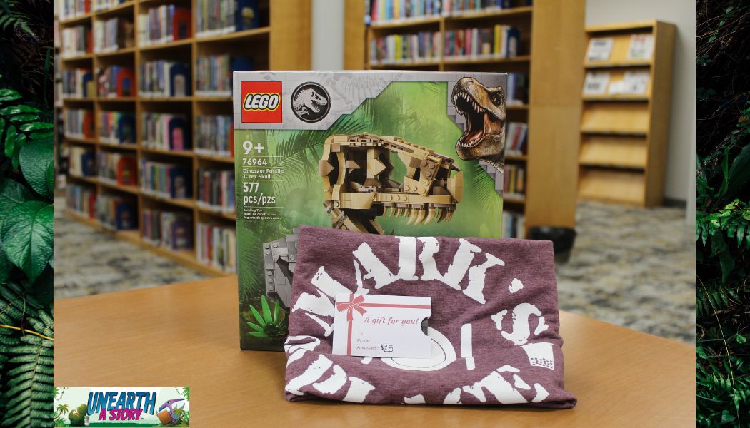 A LEGO Jurassic World T. rex set and a maroon T-shirt with a gift tag are displayed on a table in a library, with bookshelves in the background. A UNEARTH A STORY logo appears in the bottom left corner.